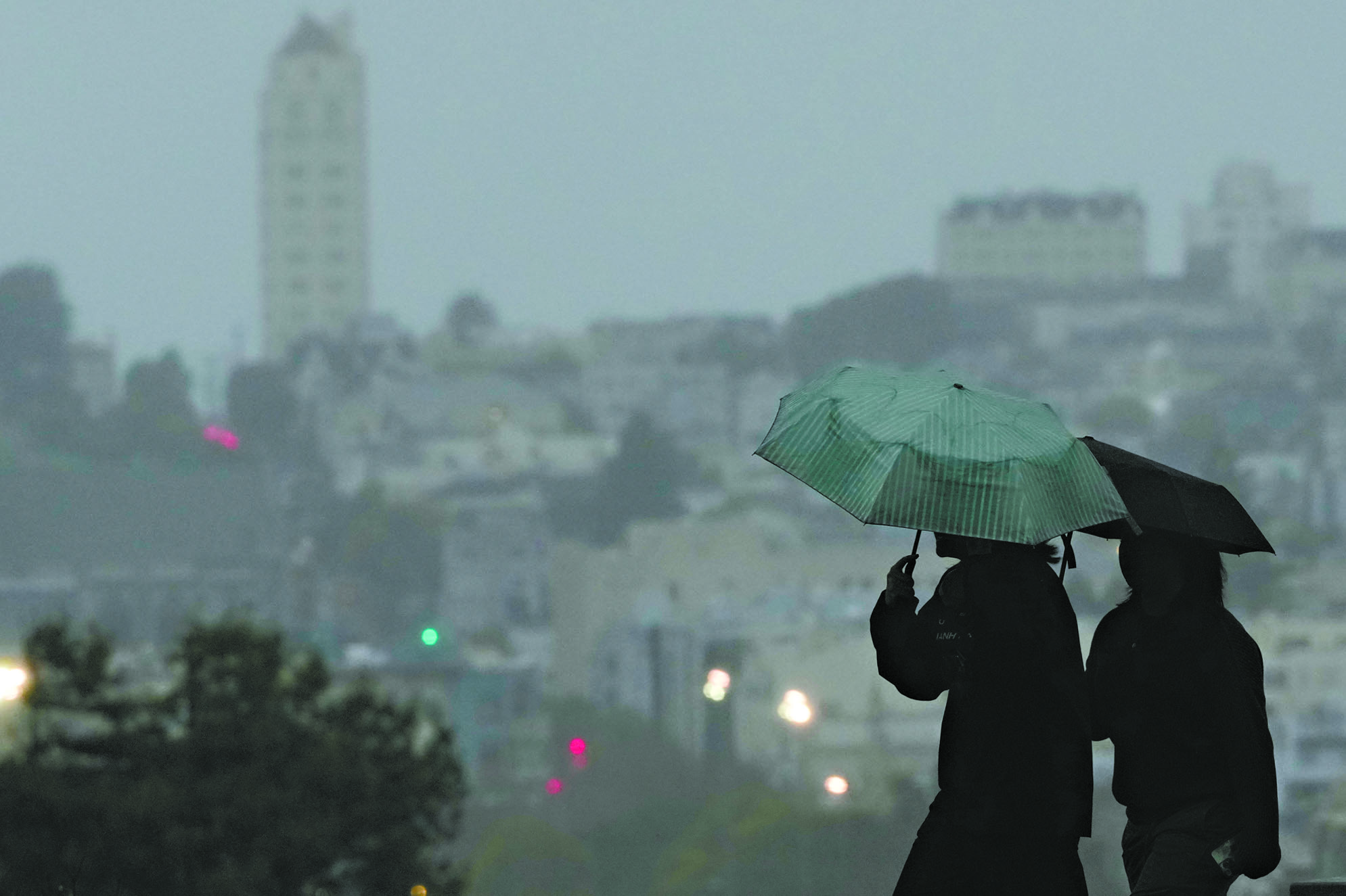 風雨來襲灣區，行人冒雨撐傘走過三藩市阿拉莫廣場公園。美聯社
