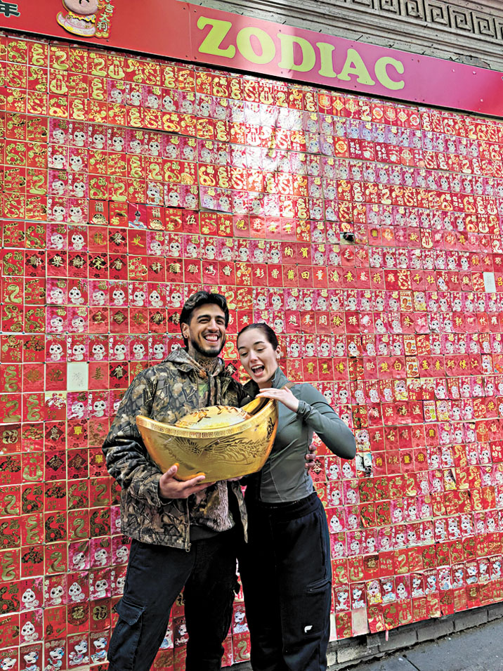 遊客在華埠生肖牆前拍照留念，手持象徵財富與祝福的金元寶，感受新年氣氛與華埠活力。記者蘇婕雅攝