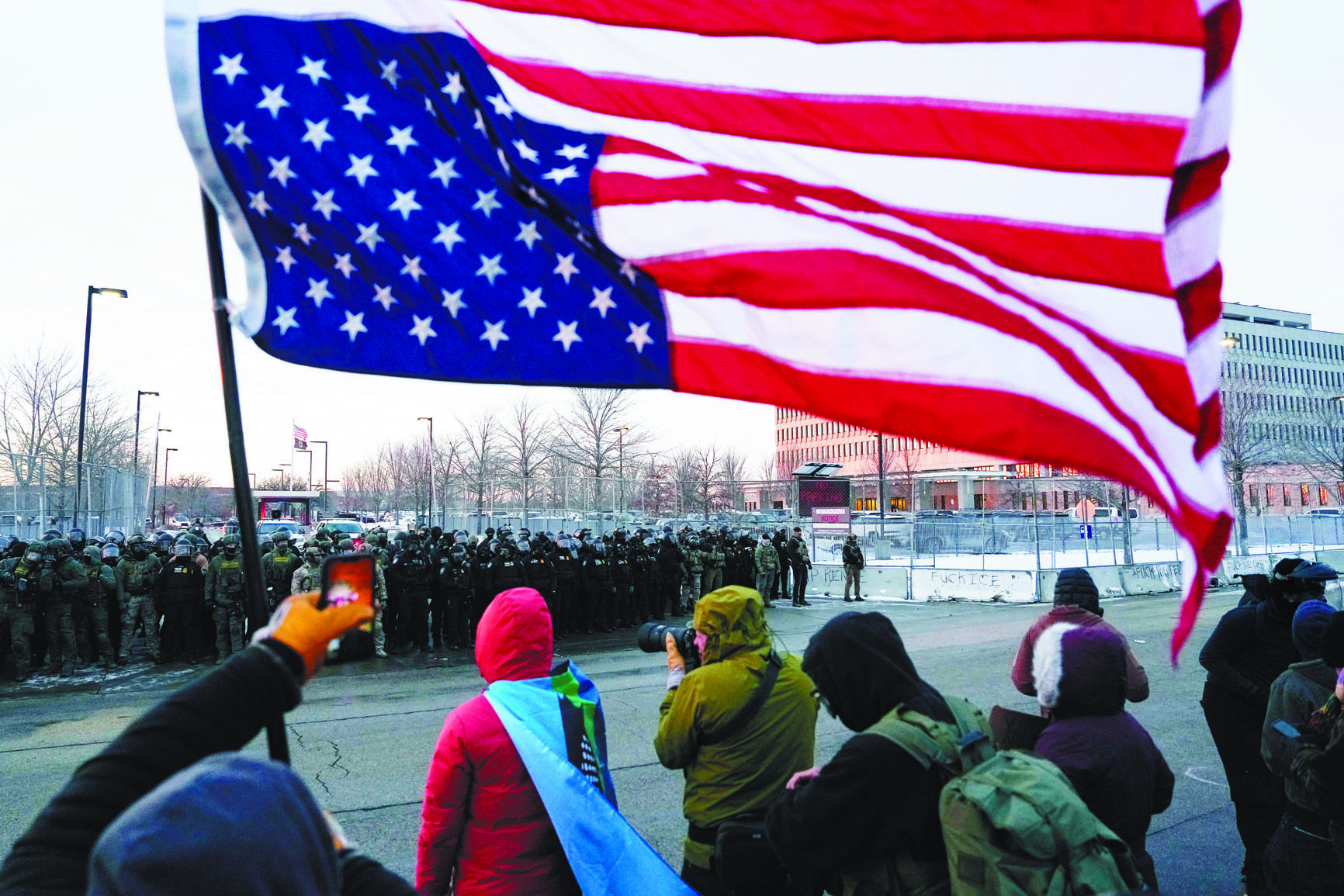 在明尼阿波利斯市聯邦大樓外，一名抗議者手持倒置的美國國旗，執法人員在一旁警戒。 美聯社